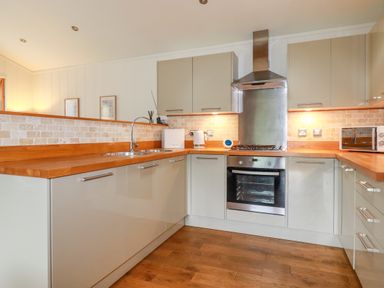 A kitchen with wooden countertops a stainless steel oven and range hood and light-colored cabinets at 10 Waters Edge in Lanreath