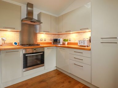 A kitchen with wooden countertops cabinets gas stove oven microwave toaster and potted plant at 10 Water's Edge Lanreath
