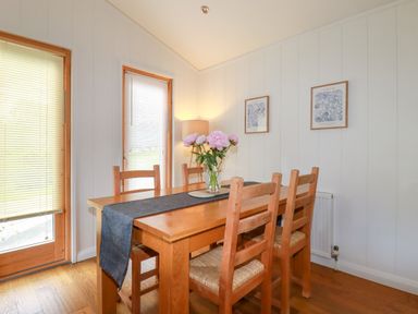 A dining room with a wooden table and chairs a vase with flowers a lamp and two framed pictures on the wall at 10 Water's Edge in Lanreath