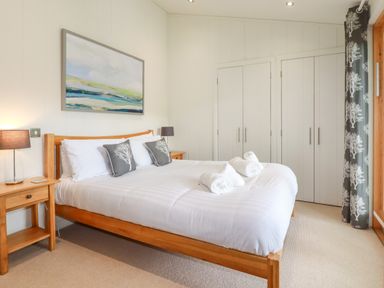 A bedroom with a wooden bed white bedding rolled towels bedside tables lamps wardrobes and a painting at 10 Water's Edge in Lanreath