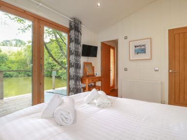 A bedroom with a bed and towels near glass doors overlooking a river at 10 Water's Edge in Lanreath