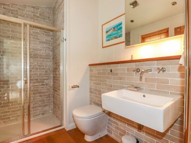 A bathroom with a shower enclosure toilet and sink with mirror and artwork at 10 Water's Edge in Lanreath
