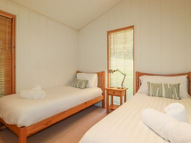 A bedroom with two single beds a wooden bedside table and window blinds at 10 Water's Edge in Lanreath