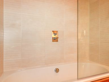A bathtub with a glass shower screen and wall-mounted controls at 10 Waters Edge in Lanreath
