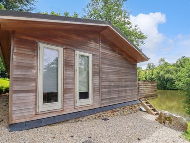 Exterior of a wooden house with two tall windows and steps leading down to a lake at 10 Water's Edge in Lanreath