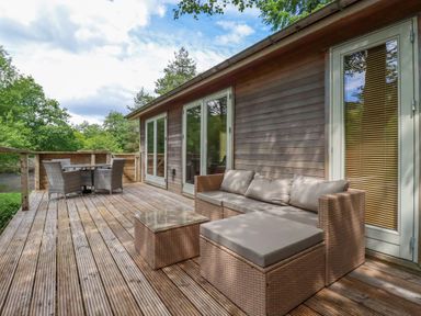 An outdoor wooden deck with wicker sofa and table and a dining set at 10 Waters Edge in Lanreath