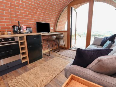 A small kitchen and living area with a gray sofa and bar stools at Rhosydd in Cyffylliog near Ruthin