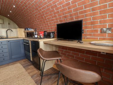A kitchen area with blue cabinets a countertop with appliances and a TV on a wooden bar with brown stools at Rhosydd in Cyffylliog near Ruthin