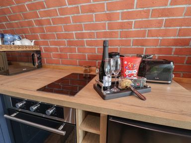 A kitchen counter with a microwave oven teapot bottle of prosecco two glasses toaster and snacks at Rhosydd in Cyffylliog near Ruthin