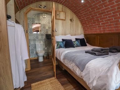 A bedroom with a bed, pillows, towels, a door leading to a bathroom with a toilet and tiled walls at Rhosydd in Cyffylliog near Ruthin