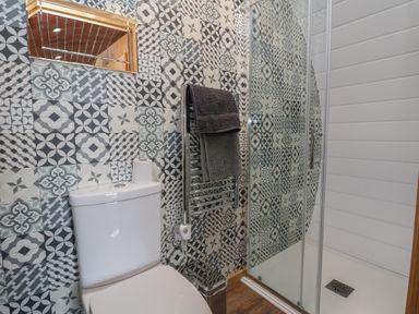 A bathroom with a toilet a glass shower enclosure a towel rail with towels and patterned wall tiles at Rhosydd in Cyffylliog near Ruthin