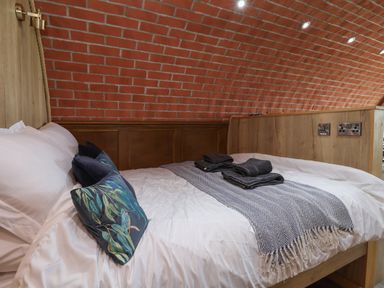 A bed with white sheets pillows and folded towels in a room with a curved brick wall at Rhosydd Cyffylliog near Ruthin