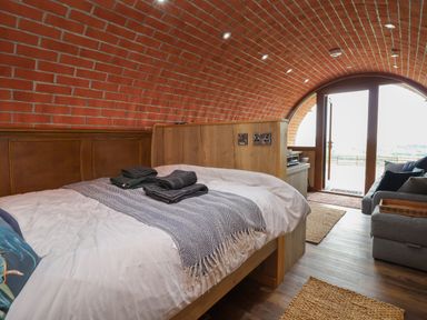 A bedroom with a wooden bed frame gray towels a sofa and a curved brick ceiling at Rhosydd in Cyffylliog near Ruthin