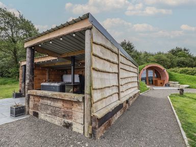 An outdoor wooden shelter with a hot tub and a fire stove next to a round brick entrance built into a hillside at Rhosydd in Cyffylliog near Ruthin