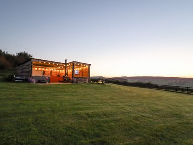 An outdoor covered seating area with string lights and a hot tub on a grassy hill at Rhosydd in Cyffylliog near Ruthin