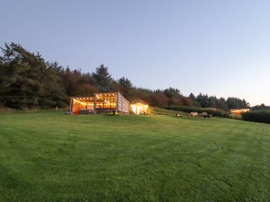 A grassy lawn with a wooden pergola and a round door building set into a hillside with trees in the background at Rhosydd in Cyffylliog near Ruthin