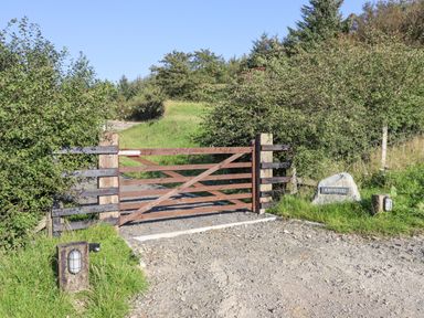 A wooden gate with gravel driveway and greenery around with a stone sign saying Rhosydd at Cyffylliog near Ruthin