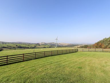 A fenced grassy field with sheep and a wind turbine in the distance at Rhosydd in Cyffylliog near Ruthin