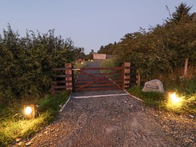 A gravel driveway with a wooden gate and two lights on either side at Rhosydd in Cyffylliog near Ruthin