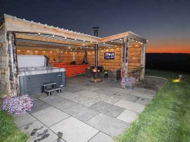 An outdoor covered patio area with a hot tub wood stove seating and a television at Rhosydd in Cyffylliog near Ruthin