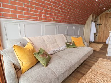 A gray sofa with yellow and green cushions in a room with brick curved wall and wooden door at Cae Bach in Cyffylliog near Ruthin
