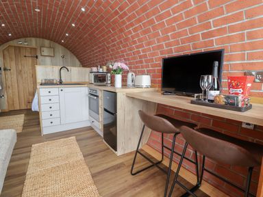 A kitchen area with white cabinets and wooden countertops next to a wooden bar with a television and two stools at Cae Bach in Cyffylliog near Ruthin