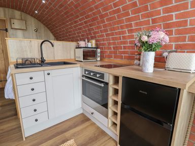 A kitchen area with white cabinets a black sink a black fridge an oven a toaster a microwave and flowers in a vase at Cae Bach Cyffylliog near Ruthin