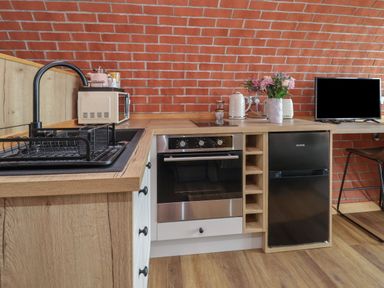 A kitchen corner with a sink drying rack microwave oven kettle flowers and a small TV at Cae Bach in Cyffylliog near Ruthin