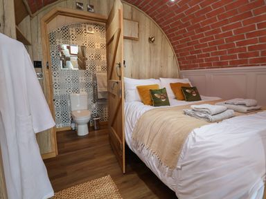 A bedroom with a bed and an open door showing a toilet and patterned wall at Cae Bach in Cyffylliog near Ruthin