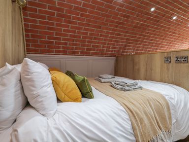 A bed with white sheets yellow and green pillows and folded towels against a brick wall at Cae Bach in Cyffylliog near Ruthin