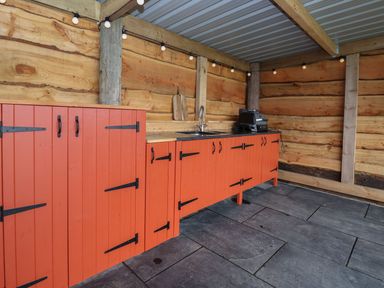 An outdoor kitchen with orange cabinets a sink a grill and wood walls at Cae Bach in Cyffylliog near Ruthin