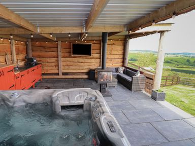 An outdoor covered patio with a hot tub seating area wood stove orange cabinets and a television at Cae Bach in Cyffylliog near Ruthin