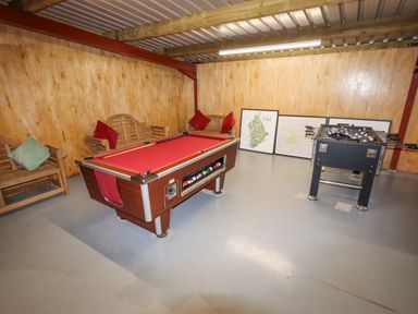 A game room with a red pool table a foosball table wooden benches and framed maps on the floor at Cae Bach in Cyffylliog near Ruthin
