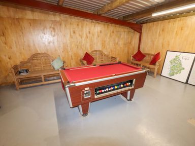A room with a pool table with red cloth and wooden benches with cushions at Cae Bach in Cyffylliog near Ruthin