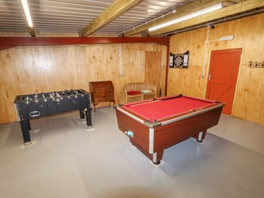 A game room with a foosball table a pool table a dartboard and a wooden bench at Cae Bach in Cyffylliog near Ruthin