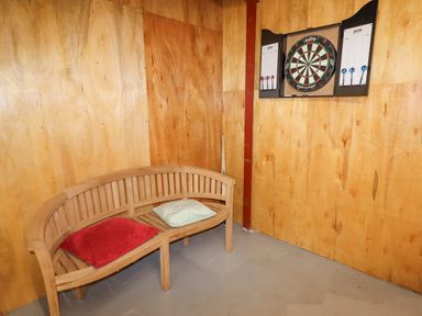 A room with plywood walls a wooden bench with cushions and a dartboard at Cae Bach in Cyffylliog near Ruthin