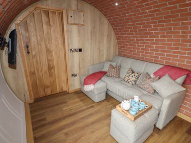 A living room with a gray sofa and ottoman with a wooden tray of cups in a room with brick and wood walls at Weirglodd in Ruthin