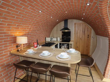 A kitchen with a curved brick ceiling a wooden countertop with four place settings and bar stools at Weirglodd in Ruthin
