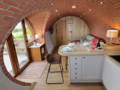 A kitchen and living area with curved brick walls a wooden countertop bar stools and a sofa at Weirglodd in Ruthin