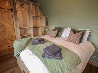 A bedroom with a bed, pillows, folded towels, wooden shelves, and a wooden door at Weirglodd in Ruthin