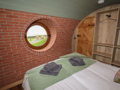 A bedroom with a round window a wooden door open shelves and towels on the bed at Weirglodd in Ruthin