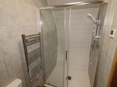 A bathroom with a glass shower enclosure a wall-mounted showerhead a chrome towel radiator and a thermostat on the wall at Weirglodd in Ruthin