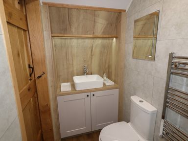 A bathroom with a wooden door a white sink a toilet a wall mirror and a chrome towel radiator at Weirglodd in Ruthin