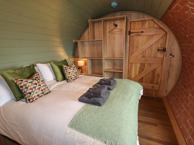 A bedroom with a bed with pillows and folded towels next to wooden shelves and a wooden door at Weirglodd in Ruthin