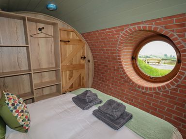 A bedroom with a bed, folded towels, circular window, wooden door and shelves at Weirglodd in Ruthin