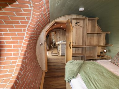 A bedroom with a bed towel and blanket in front of shelves in a tunnel shaped room at Weirglodd in Ruthin