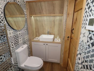 A bathroom with a toilet a circular mirror a white sink with cabinet wood paneling and patterned wall tiles at Weirglodd in Ruthin