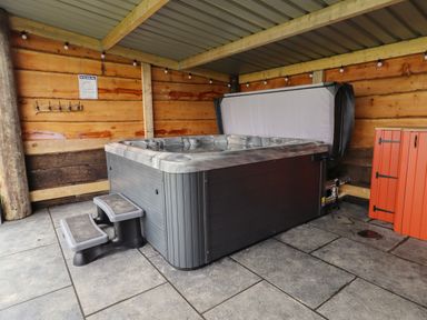 A hot tub with steps under a covered wooden structure with string lights and an orange cabinet at Weirglodd in Ruthin