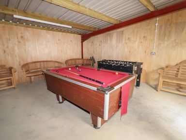 A game room with a pool table, foosball table, and wooden benches at Weirglodd in Ruthin