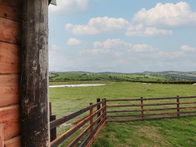 A view of green fields with a wooden fence and a pond from a wooden structure at Weirglodd in Ruthin